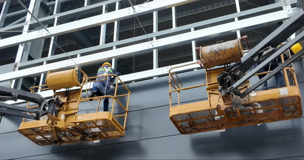 Steel building project progress with workers installing exterior wall panels on site